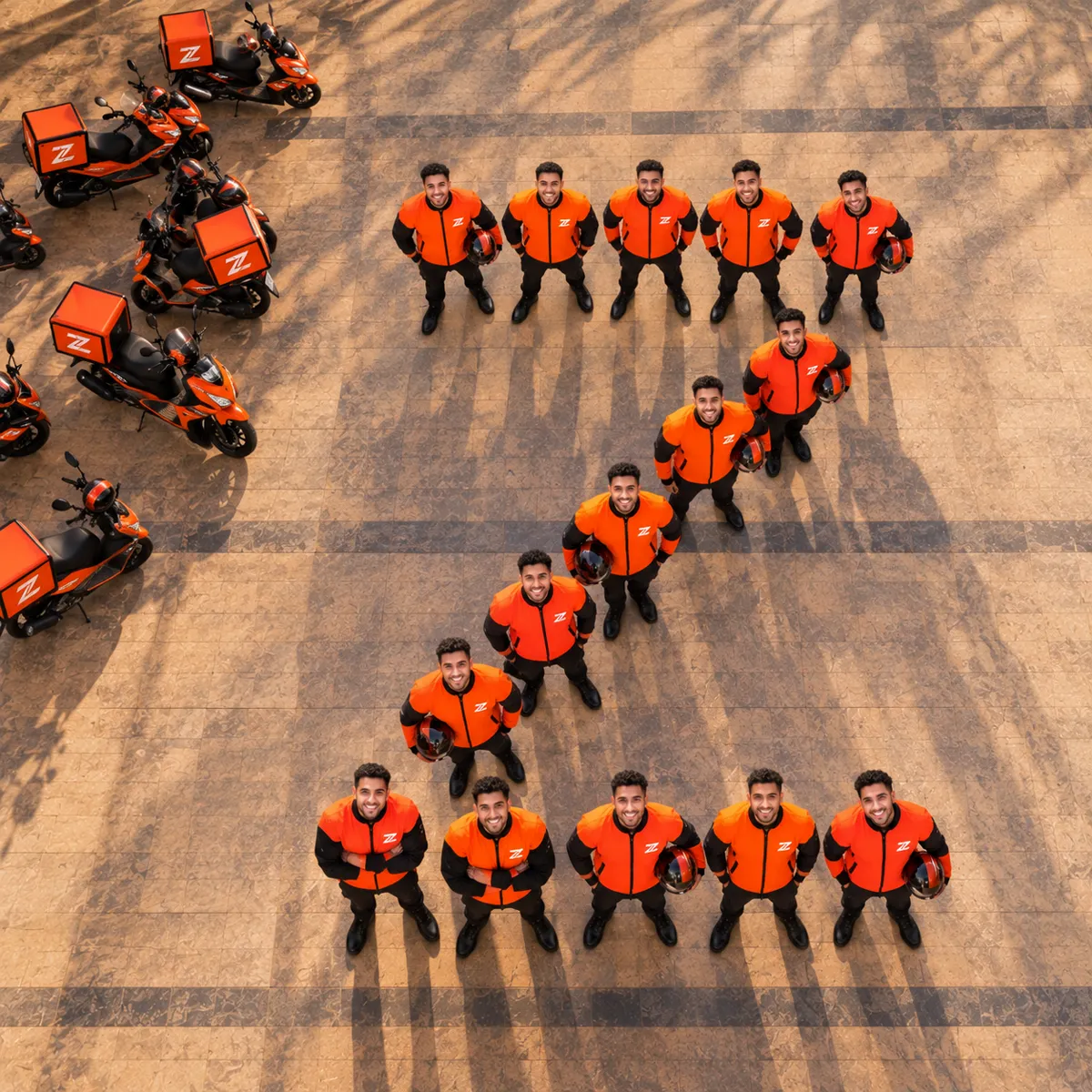 Lahazat couriers in orange uniforms standing in the shape of a Z beside their delivery scooters